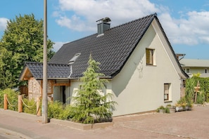 A single-story house with a sloped roof, a chimney, and a small porch with a wooden railing.