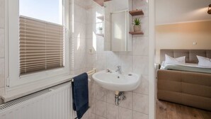 Uma casa de banho com janela, lavatório e cama.