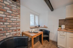 Cocina compacta con pared de ladrillo, una mesa de madera, dos sillas, un ventanal y un armario blanco.