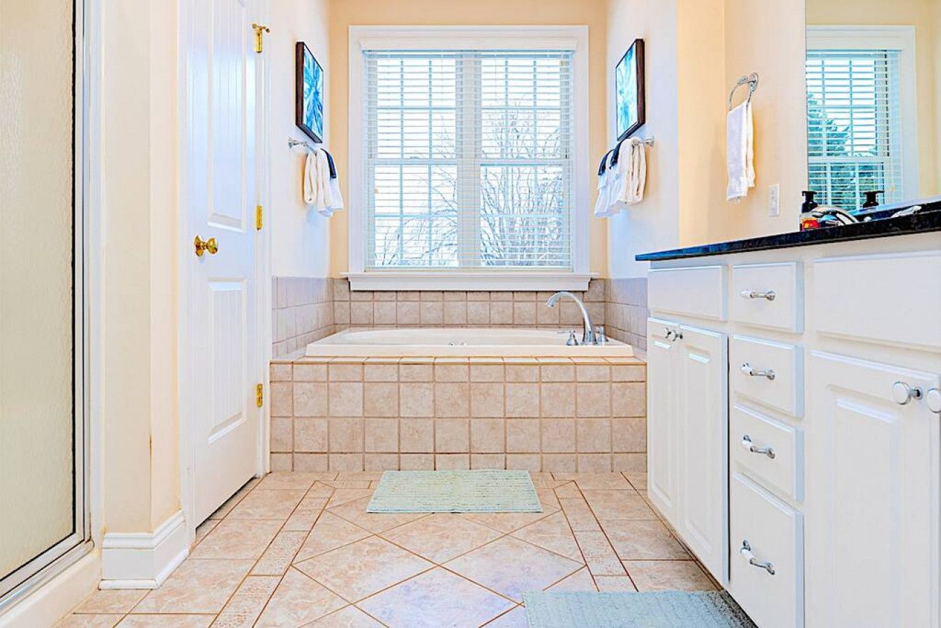 A bathroom with a bathtub, a window with blinds, and a sink.