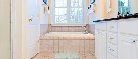 A bathroom with a bathtub, a window with blinds, and a sink.