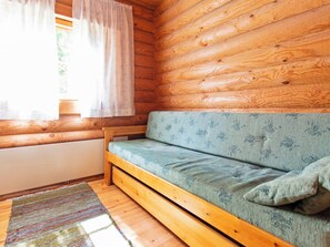 Interior de una cabaña de madera con sofá, una ventana con cortinas y una alfombra estampada.