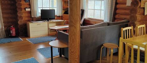 A log cabin interior with a sofa, dining table, chairs, a television, and a fireplace.