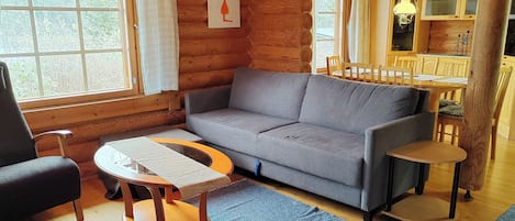 L’intérieur d’un chalet confortable, avec un canapé gris, une petite table ronde et un coin repas doté de chaises en bois.