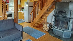 A cozy cabin interior with a wooden staircase, a fireplace, a kitchen area, and a sofa. - Heinäsorsa by Interhome (Joutsa)