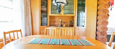 Une table à manger en bois avec des chaises, un luminaire suspendu et un coin cuisine avec des meubles en bois et un fourneau.