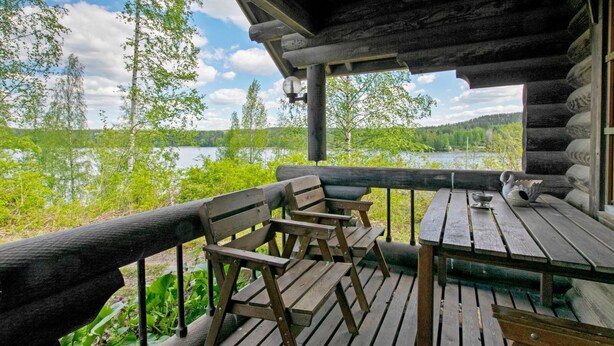 A wooden deck with benches and a table, overlooking a lake with trees and hills in the background. - Heinäsorsa by Interhome (Joutsa)