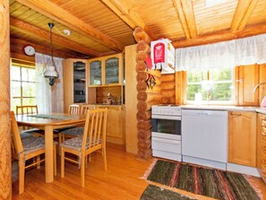 A wooden interior with a dining table, chairs, a kitchen with a stove and oven, and a window with curtains. - Heinäsorsa by Interhome (Joutsa)