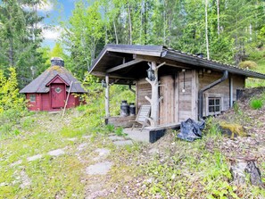 A rustic cabin with a porch, a red shed, and a forested backdrop.