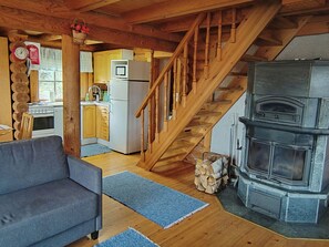 A cozy cabin interior with a wooden staircase, a sofa, a kitchen area, and a wood-burning stove. - Heinäsorsa by Interhome (Joutsa)
