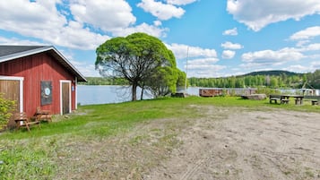 A red barn with a door and windows, a large tree in front, and a lake in the background.