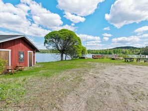 A red barn with a door and windows, a large tree in front, and a lake in the background. - Heinäsorsa by Interhome (Joutsa)