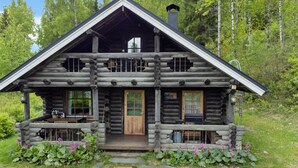 A log cabin with a front porch, a chimney, and a window overlooking a forested area. - Heinäsorsa by Interhome (Joutsa)