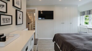 A bedroom with a bed, a TV mounted on the wall, a desk with a chair, and a wardrobe. - Hedigen Hüs - Our Hedigen Hüs impresses with its consistent furnishings in the Sylt style. (Sylt)