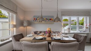 A dining area with a wooden table set for four, surrounded by chairs. There are two pendant lights above the table, and a painting hangs on the wall. - Hedigen Hüs - Our Hedigen Hüs impresses with its consistent furnishings in the Sylt style. (Sylt)