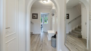 A hallway with white walls, wooden flooring, a staircase, and a large mirror. - Hedigen Hüs - Our Hedigen Hüs impresses with its consistent furnishings in the Sylt style. (Sylt)