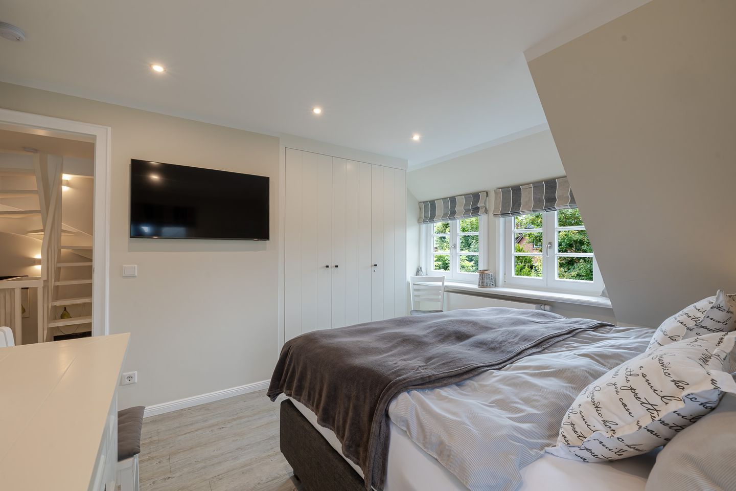 Une chambre à coucher comprenant un lit, un téléviseur fixé au mur, une fenêtre avec des rideaux et une armoire intégrée.