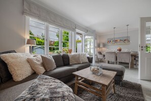 Un salon moderne avec un canapé gris, une table basse en bois et un coin repas comprenant une table et des chaises blanches.