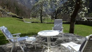 Un patio exterior con suelo de piedra, sillones blancos y una mesa redonda.