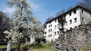 Un edificio de piedra tradicional con numerosas ventanas y balcones, rodeado de un muro de piedra y un pequeño jardín.