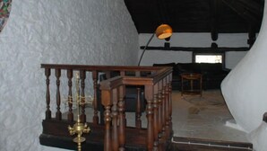 Una habitación con pared blanca con textura, una escalera de madera con barandilla, un candelabro de bronce y una lámpara de pie.