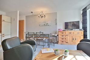 Un soggiorno moderno con zona pranzo, un mobiletto in legno con televisore e un lampadario.