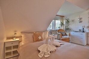 Ein Schlafzimmer mit einem Bett, einem Nachttisch, einer Kommode, einem Sessel und einem Fenster.