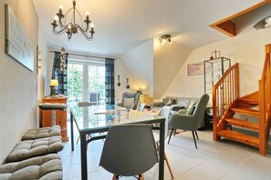 Un soggiorno moderno con un tavolo da pranzo in vetro, divani grigi, una scala in legno e un lampadario.