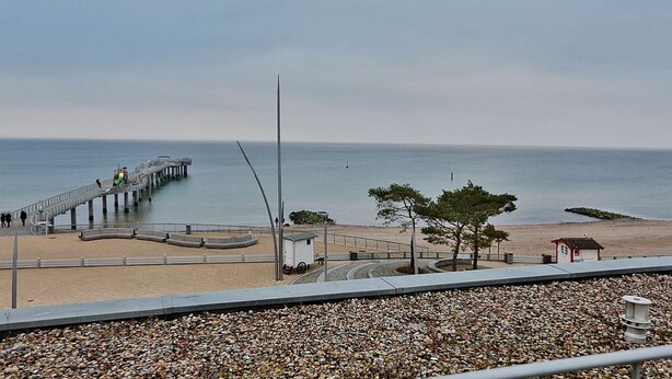 A coastal view with a pier extending into the sea, a sandy beach, and a small structure near the water's edge.