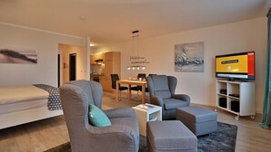 A modern living room with a sofa, armchairs, a TV, and a dining area.