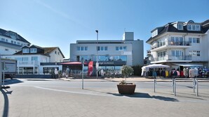 A coastal promenade with a central building, shops, and outdoor seating areas.
