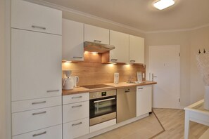 A modern kitchen with white cabinetry, a built-in oven, and a coffee maker. - Wohnpark am Mühlenteich Apartment 17 - Wohnpark am Mühlenteich (Timmendorfer Strand)
