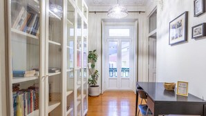 A hallway with a wooden floor, a potted plant, a table with a chair, and a bookshelf with books. - Cozy Lisbon Stay - 2 Min Walk from Av. Liberdade by Lisbeyond (Lisboa)