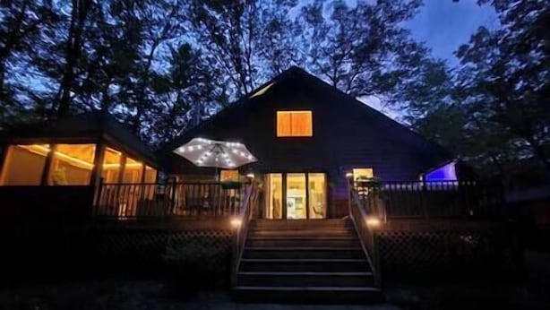 A cabin with a porch, a staircase leading to the entrance, and a window with lights on.
