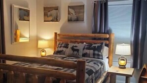 A wooden bed with a plaid bedspread and a deer pillow, flanked by two bedside lamps.