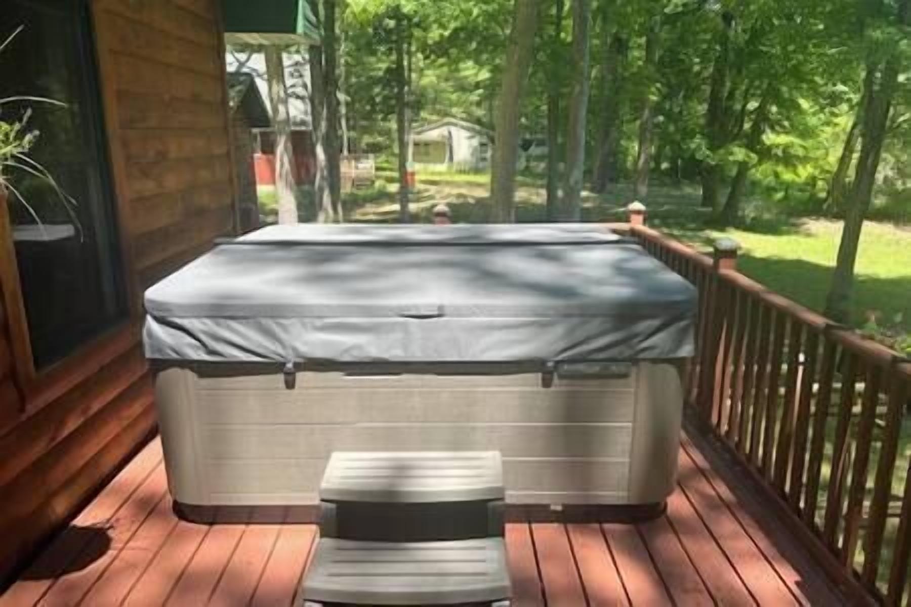 A hot tub on a wooden deck with a view of trees and a house in the background.