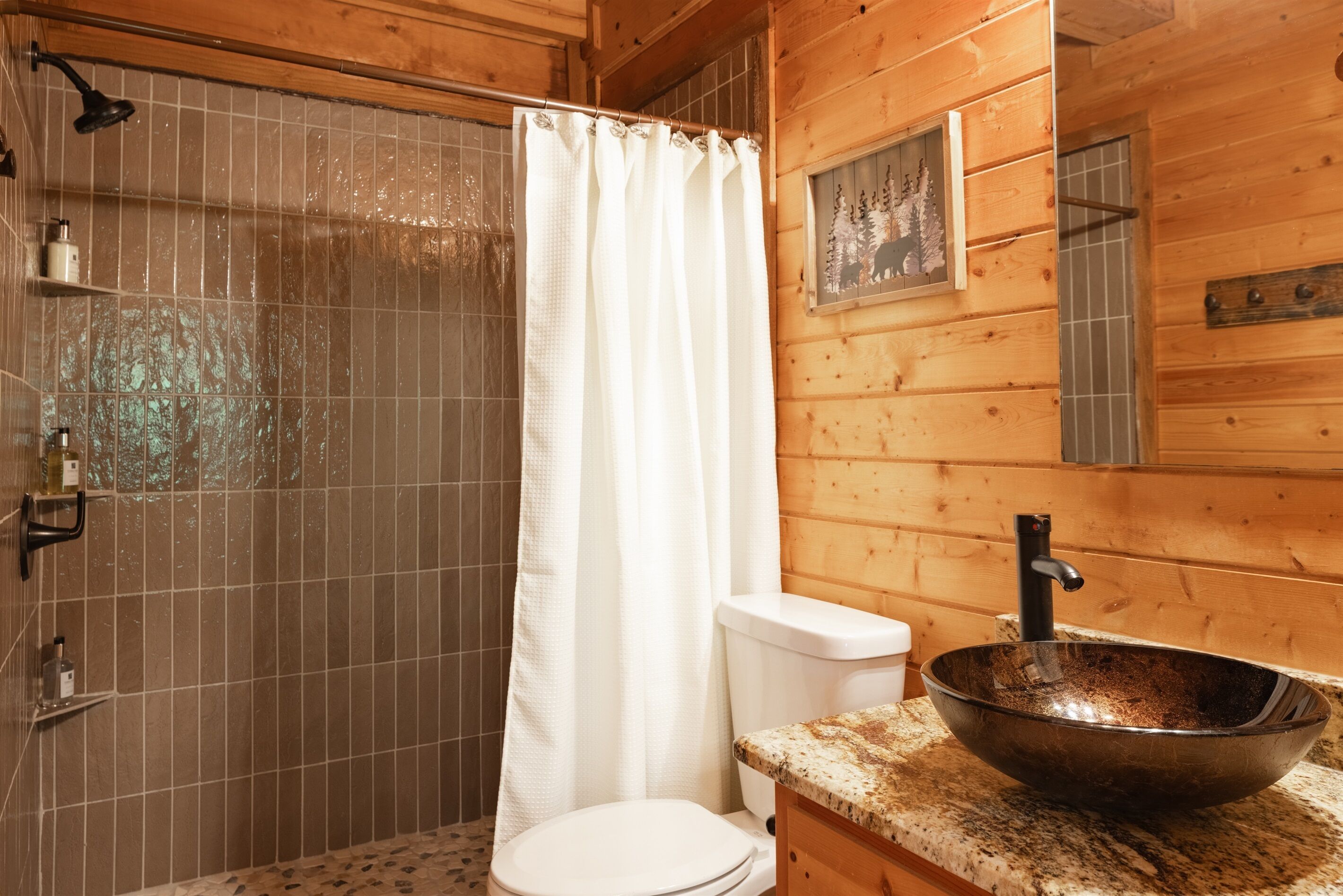 A wooden cabin bathroom with a shower, toilet, and a large bowl sink.