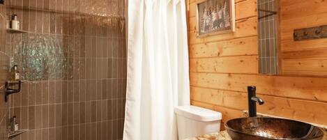 A wooden cabin bathroom with a shower, toilet, and a large bowl sink.