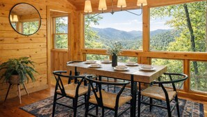 Uma cabana de madeira com uma mesa de jantar posta para quatro pessoas, cercada por grandes janelas com vista para as montanhas.