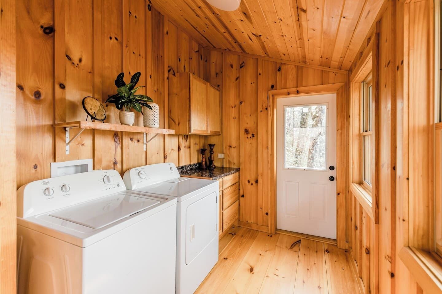 Ein gemütliches Holzhaus mit Waschküche, einschließlich Waschmaschine und Trockner, Holzwänden und einer Tür mit Fenster.
