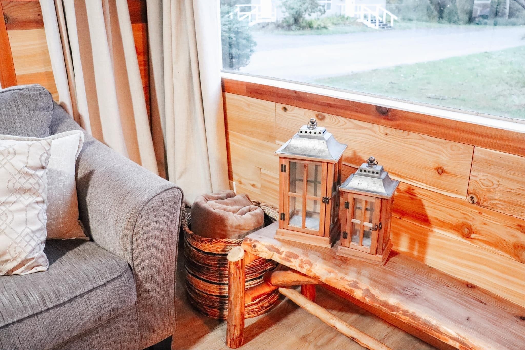 A cozy room with a wooden bench, a cushioned bench, and a small wooden table with two lanterns.