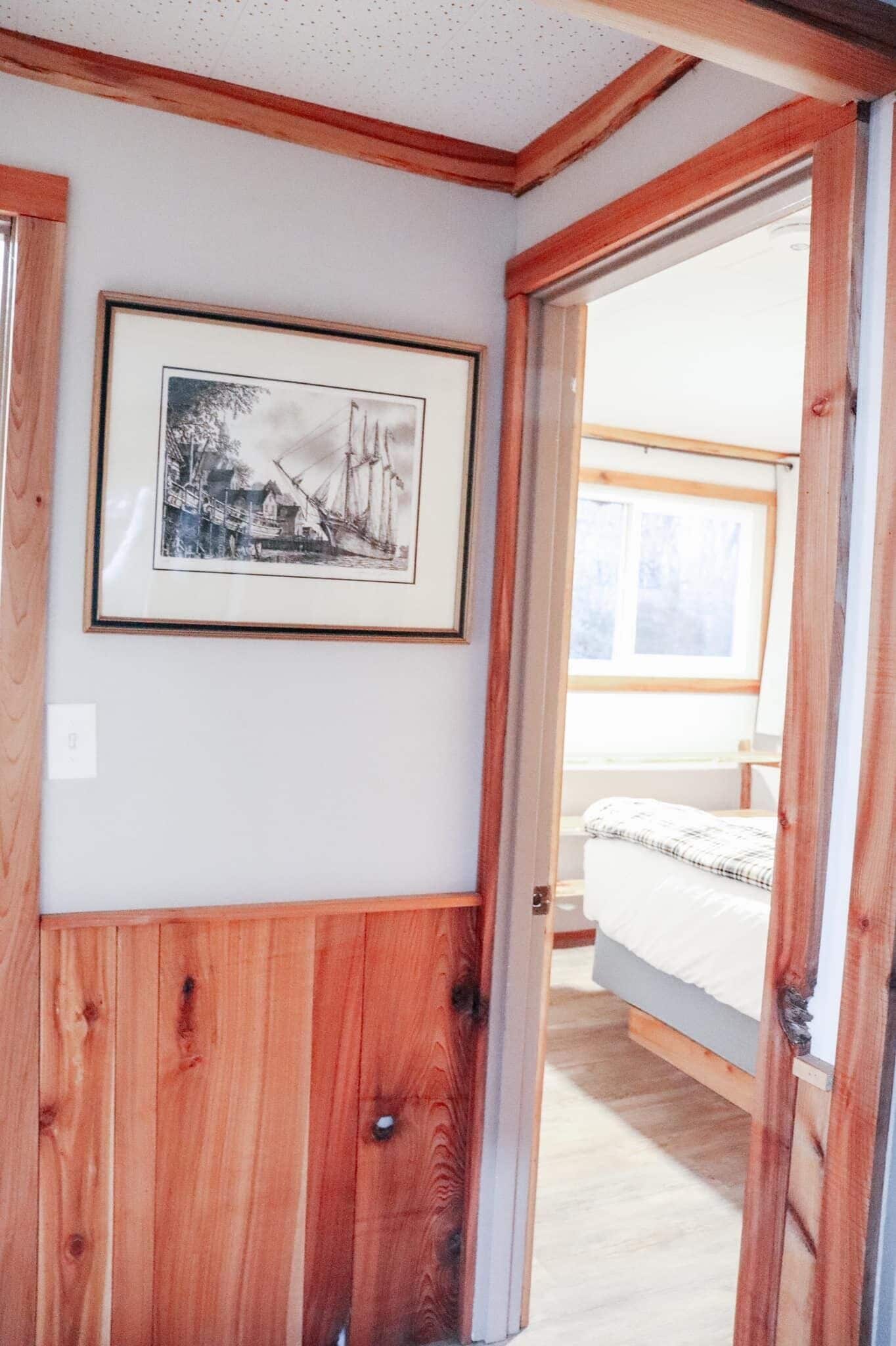 A wooden-paneled room with a framed picture on the wall, a bed, and a window.