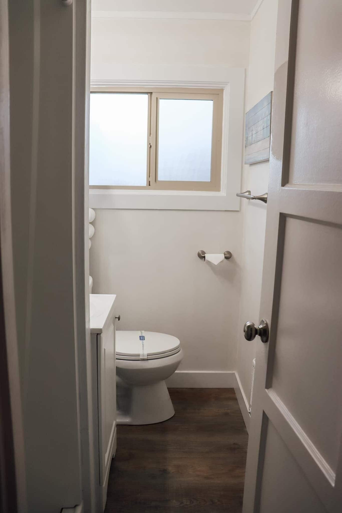 A bathroom with a toilet, a window above it, and a towel rack.