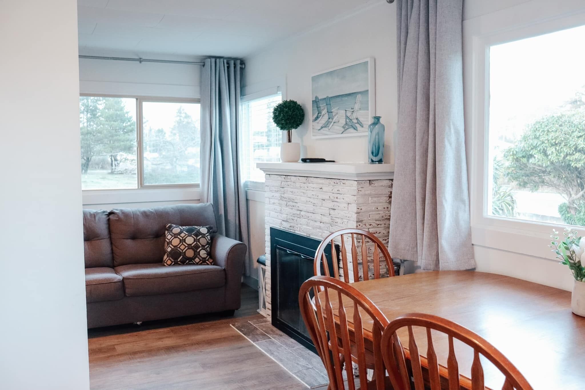 A living room with a sofa, a fireplace, a dining table with chairs, and a window with curtains.