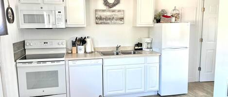Una cocina con armarios blancos, microondas, cafetera y refrigerador.