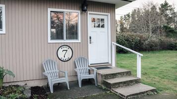 A cabin with two Adirondack chairs outside, a white door, and a number '7' sign on the wall.