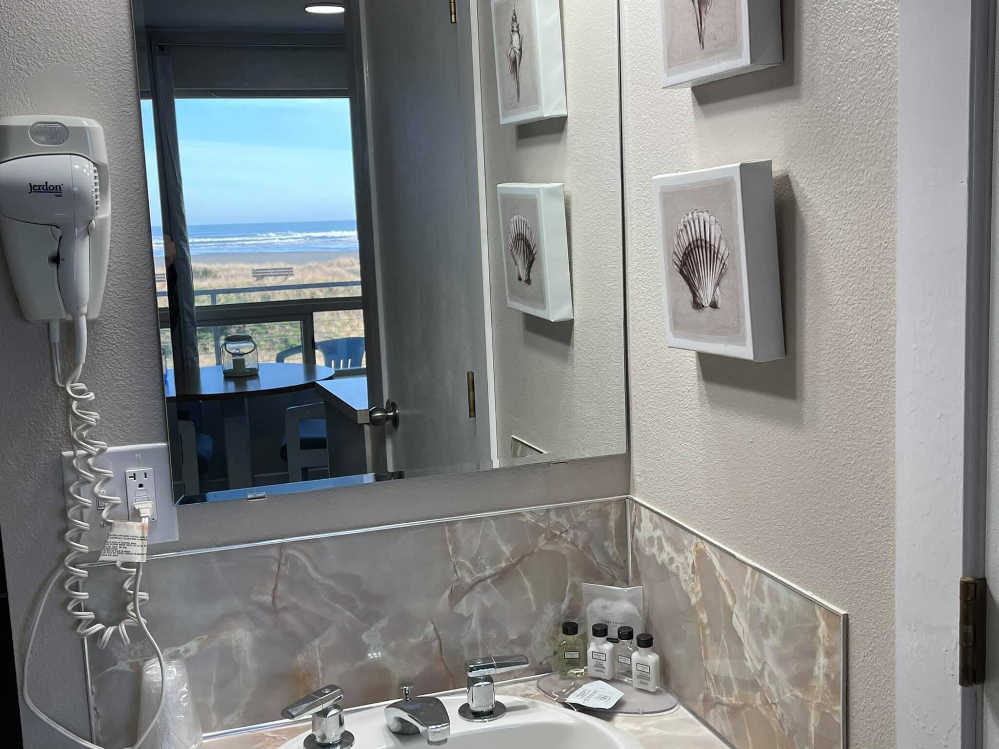 A bathroom with a hairdryer, a sink, and a view of the beach.