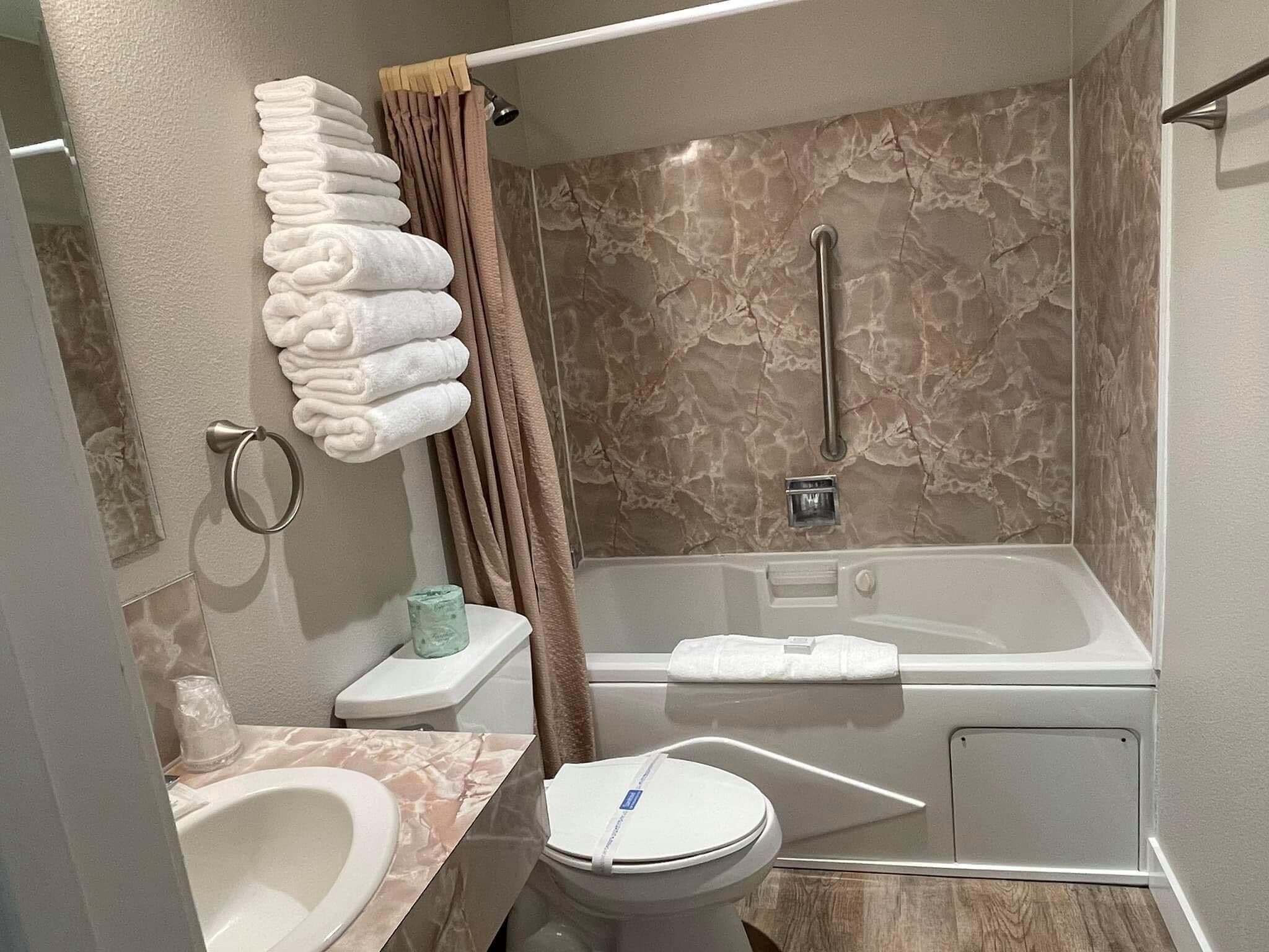 A bathroom with a bathtub, toilet, sink, and a towel rack with folded towels.