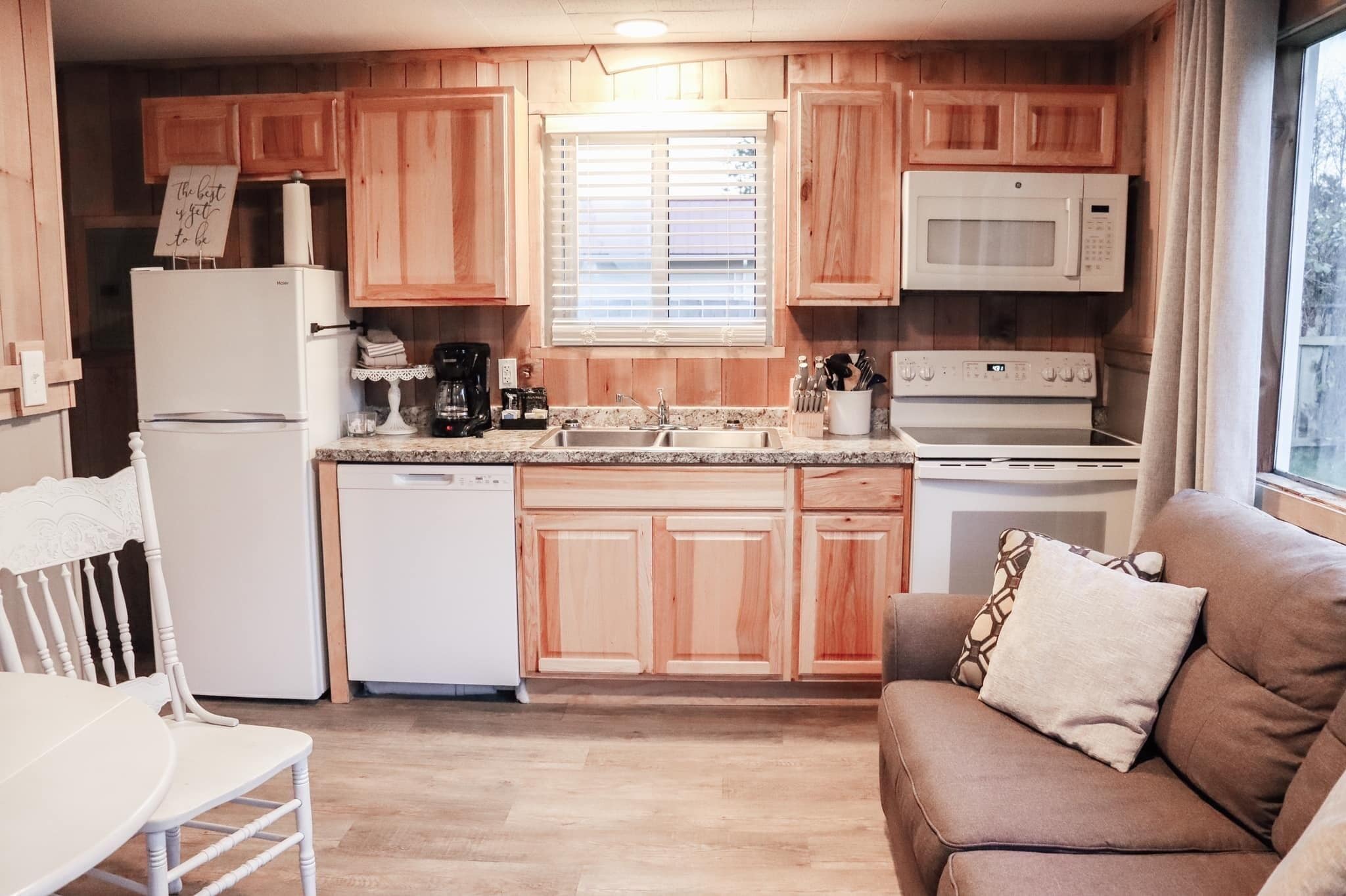 Una cocina compacta con armarios de madera, un refrigerador blanco, microondas, lavavajillas y un comedor con mesa y sillas.