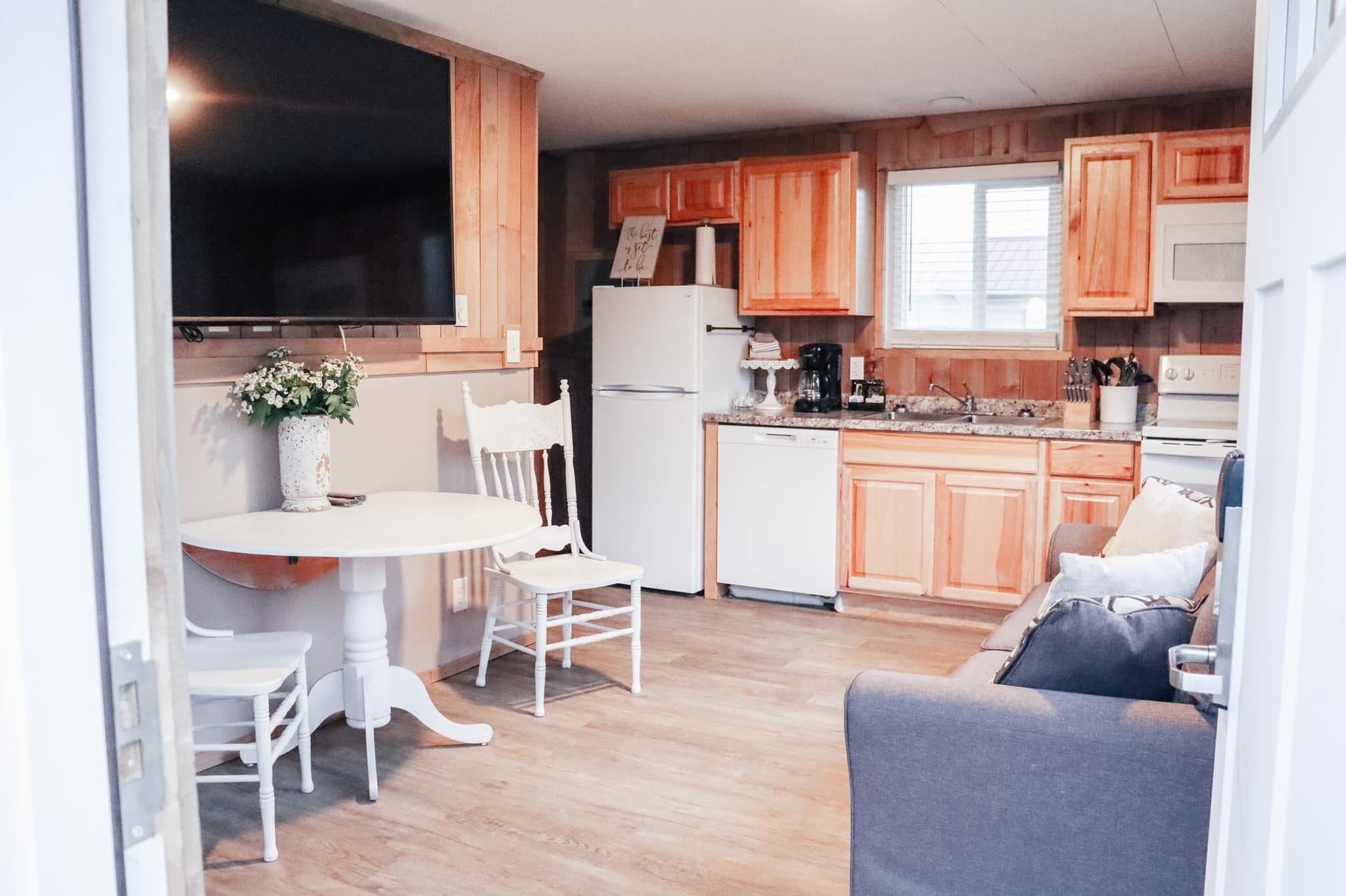 Una cocina compacta con armarios de madera, un refrigerador blanco, una mesa de comedor con sillas y un sofá en la sala.